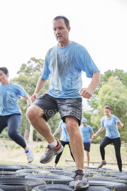 Determined man jumping tires on boot camp obstacle course — Stock Photo