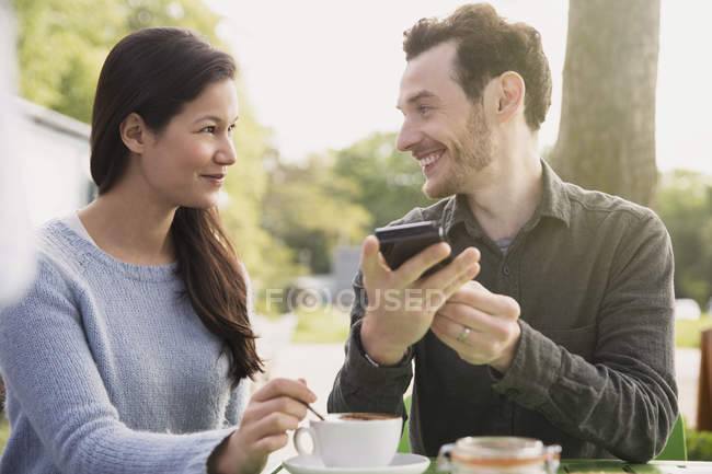 Casal com telefone celular bebendo café no café ao ar livre — Fotografia de Stock