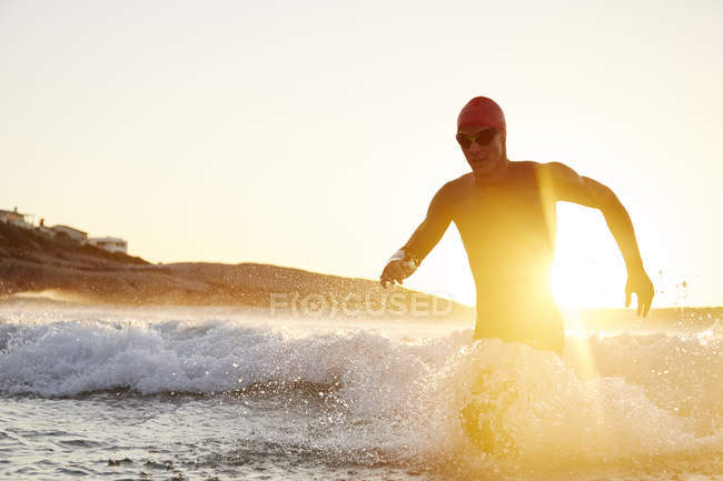 Чоловічий тріатлоніст плаває у вологому костюмі, що біжить з сонячного океану — стокове фото