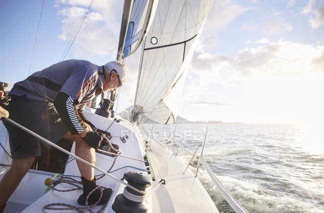 Uomo vela tirando sartiame sulla barca a vela sull'oceano soleggiato — Foto stock