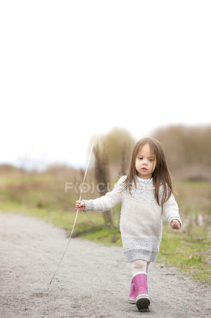 Girl in pink rain boots walking with stick — Stock Photo