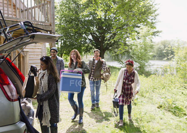 Friends loading cooler and belongings into car outside sunny cabin — Stock Photo