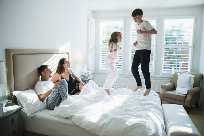 Parents watching children jumping on bed — Stock Photo