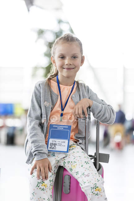 Portrait smiling girl sitting on suitcase in airport — Stock Photo