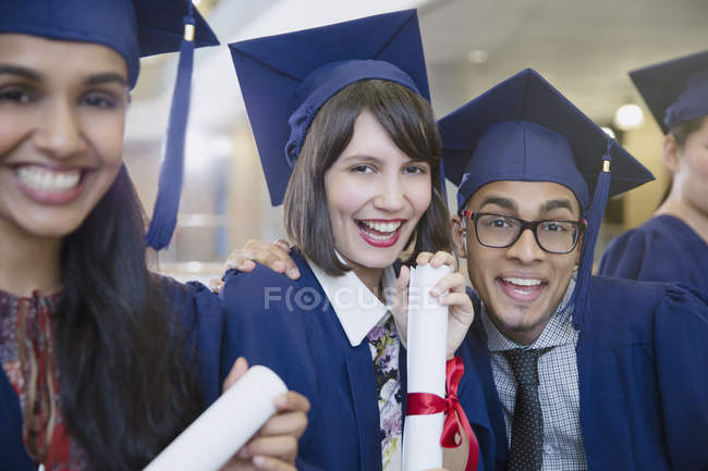 Портрет захоплених випускників коледжу в шапці і сукні позує з дипломом — стокове фото