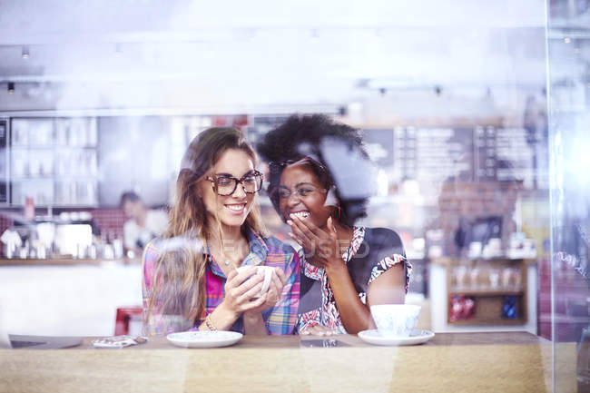 Mulheres rindo e bebendo café na janela do café — Fotografia de Stock