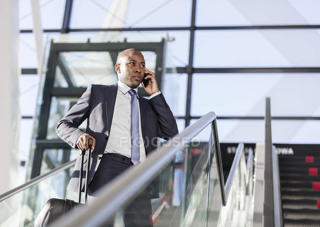 Бизнесмен разговаривает по мобильному телефону на эскалаторе аэропорта — стоковое фото