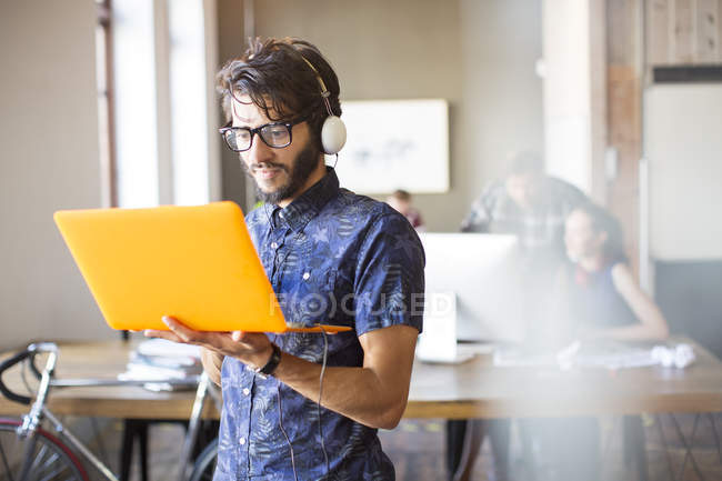 Випадковий бізнесмен носить навушники і використовує ноутбук в офісі — стокове фото