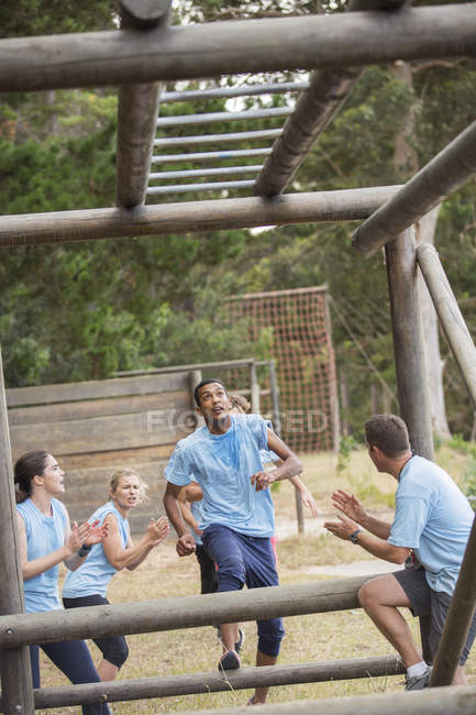 Teammates cheering for man nearing monkey bars on boot camp race course — Stock Photo