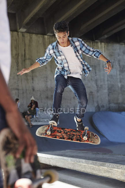 Focused teenage boy flipping skateboard at skate park — Stock Photo