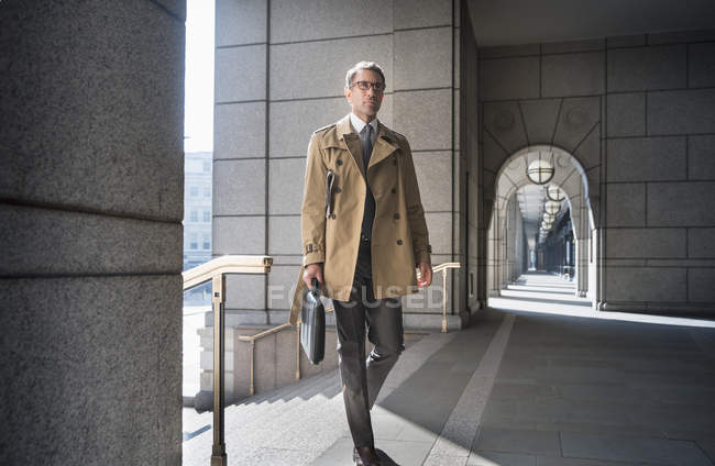 Empresário corporativo em casaco de trincheira andando no claustro — Fotografia de Stock