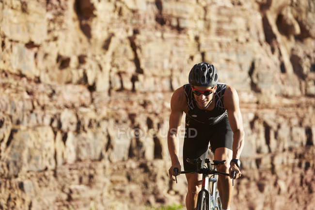 Male triathlete cyclist cycling along sunny rocks — Stock Photo