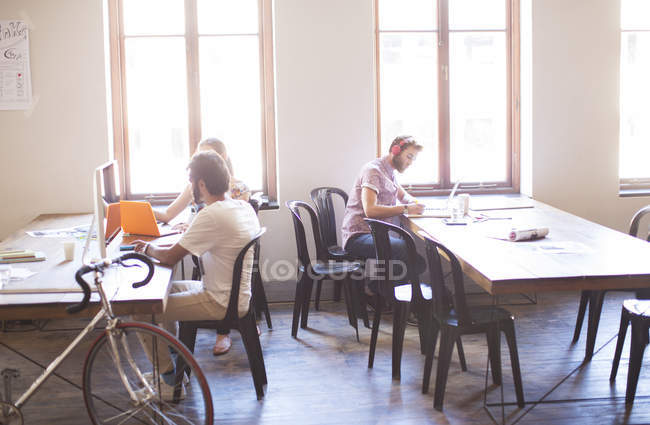 Des gens d'affaires créatifs travaillant aux tables dans un bureau ensoleillé — Photo de stock
