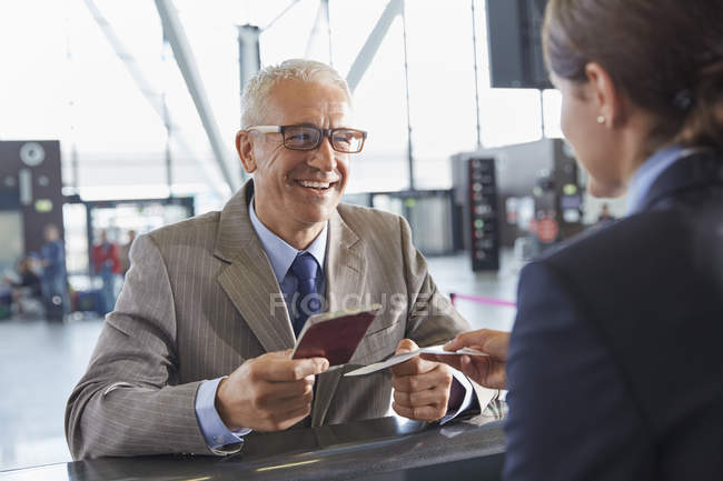 Empresário sorrindo dando passaporte ao representante de atendimento ao cliente no balcão de check-in do aeroporto — Fotografia de Stock