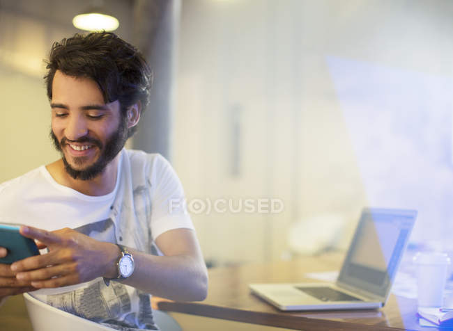 Smiling casual businessman texting with cell phone in office — Stock Photo