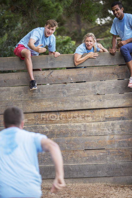 Teammates at wall cheering man on boot camp obstacle course — Stock Photo