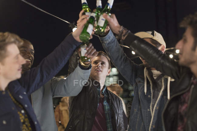 Giovani uomini brindare bottiglie di birra alla festa — Foto stock