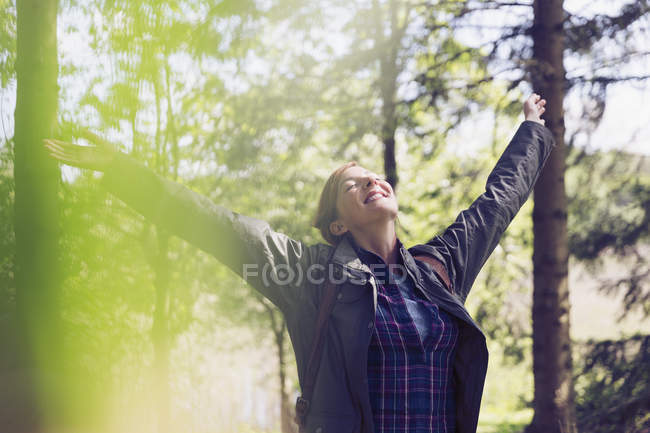 Exuberant woman hiking smiling with arms raised and head back in sunny woods — Stock Photo