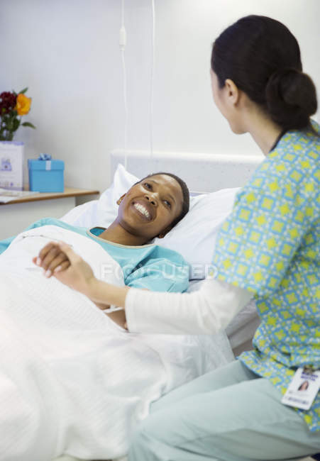 Nurse holding smiling patients hand in hospital room — Stock Photo