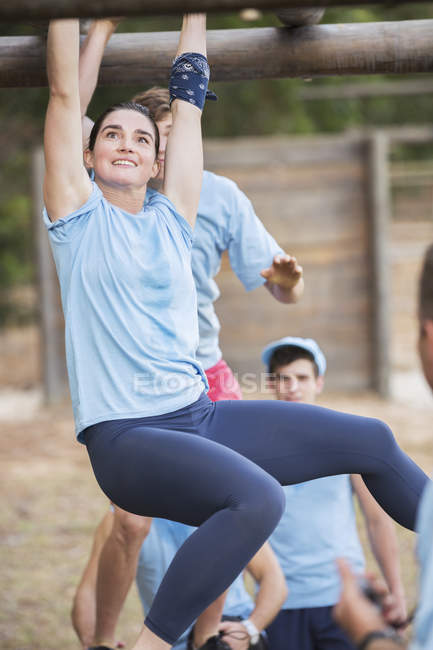 Smiling woman crossing monkey bars at boot camp — Stock Photo