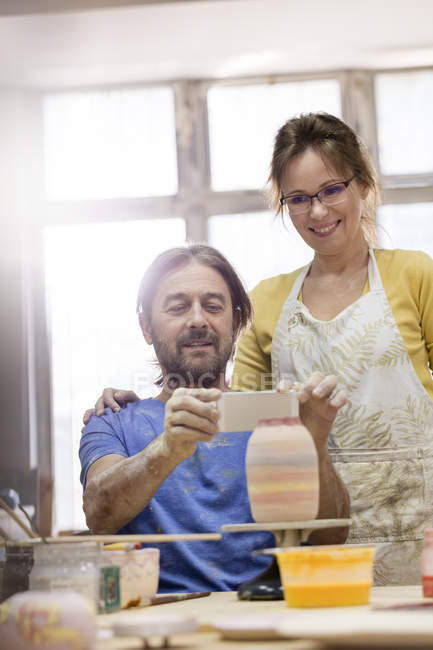 Mature couple photographing pottery vase with camera phone in studio — Stock Photo