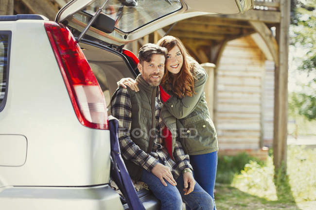 Portrait smiling couple at back of car outside cabin — Stock Photo