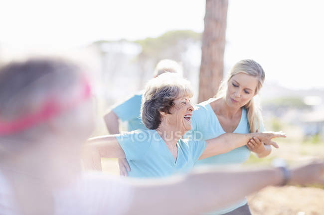 Instructora de yoga guiando a una mujer mayor en un parque soleado - foto de stock