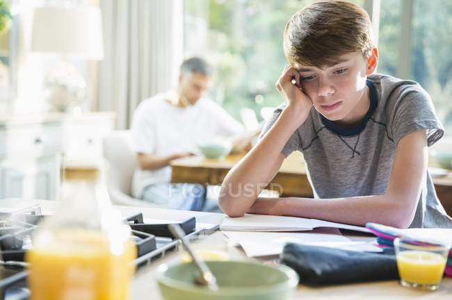 Разочарованный мальчик делает домашнее задание за завтраком — стоковое фото