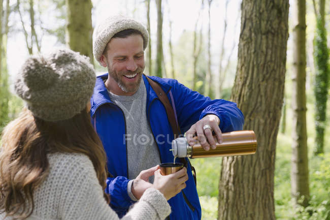 Пара походов и питье кофе из контейнера с изолированными напитками в лесу — стоковое фото
