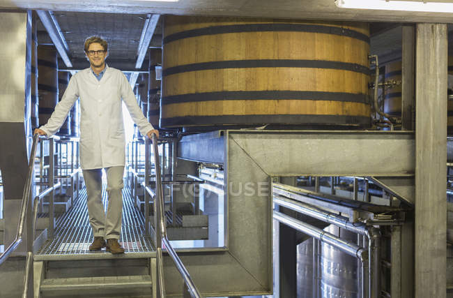Portrait confident vintner in lab coat on platform in winery cellar — Stock Photo