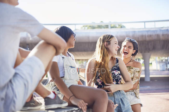 Adolescentes riendo pasando el rato en el parque de skate soleado - foto de stock