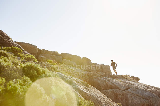 Coureur triathlète masculin courant sur un sentier rocheux ensoleillé — Photo de stock