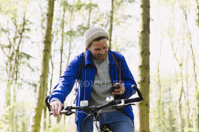 Man mountain bike mensagens de texto com telefone celular na floresta — Fotografia de Stock