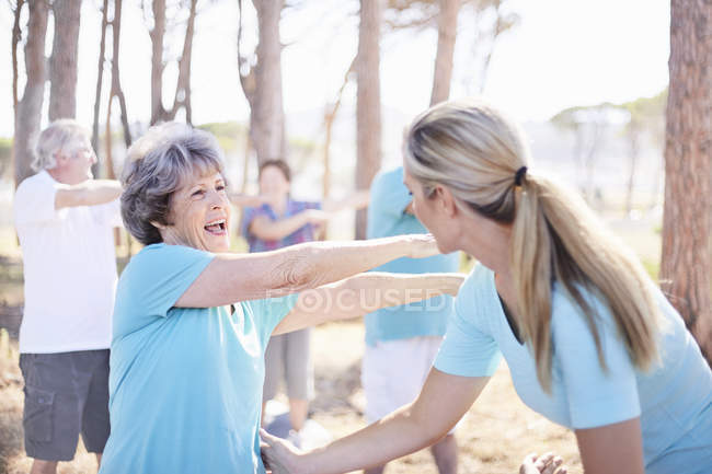 Instructora de yoga guiando a una mujer mayor en el parque - foto de stock