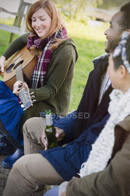 Femme jouant de la guitare avec des amis boire de la bière — Photo de stock