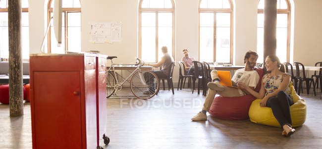 Pessoas de negócios casuais trabalhando no laptop em cadeiras de saco de feijão em escritório aberto — Fotografia de Stock