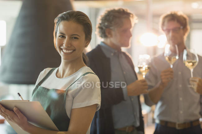 Retrato mujer sonriente con portapapeles trabajando en sala de degustación de vinos - foto de stock