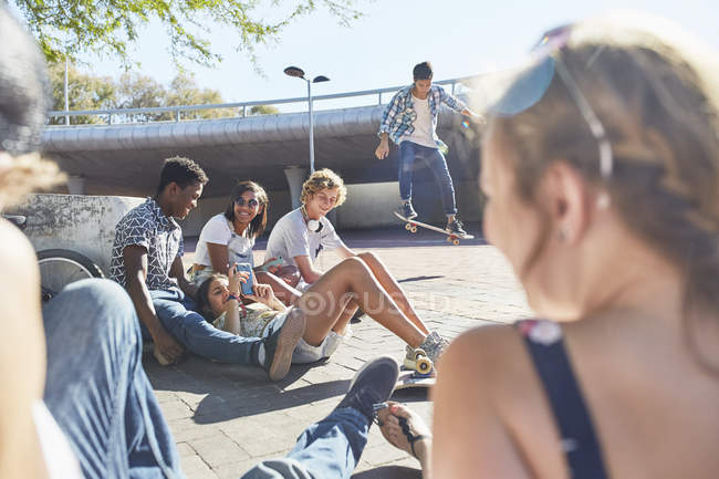 Amigos adolescentes pasando el rato patinando en el soleado parque de skate - foto de stock