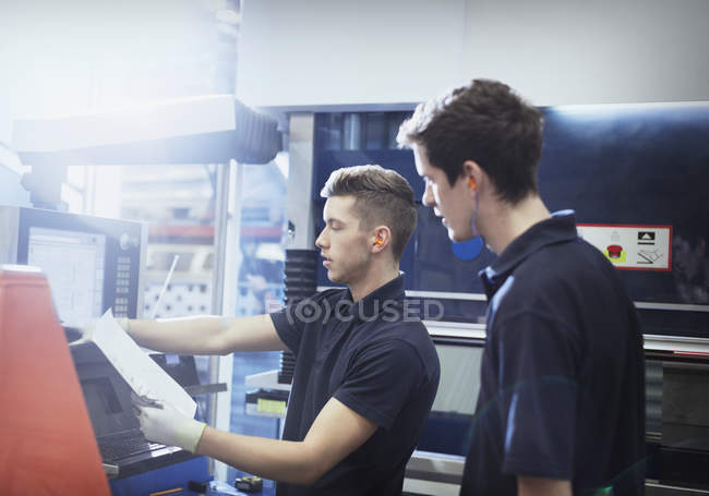 Trabajadores con portapapeles en el panel de control de maquinaria en la fábrica de acero - foto de stock