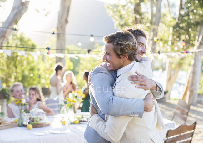 Наречений і кращий чоловік обіймається під час весільного прийому в саду — стокове фото