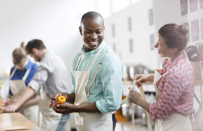 Smiling woman tying apron for man in cooking class kitchen — Stock Photo