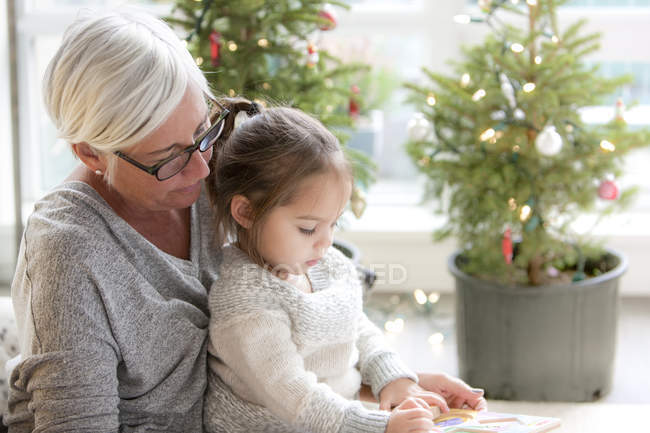 Grandmother watching granddaughter drawing in front of Christmas trees — Stock Photo