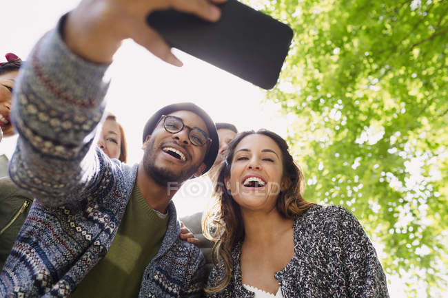 Amigos entusiastas tomando selfie con el teléfono de la cámara debajo del árbol - foto de stock