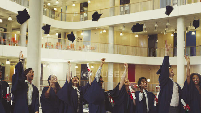Graduados universitarios lanzando gorra juntos - foto de stock