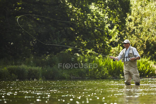 Uomo anziano pesca a mosca al fiume estivo — Foto stock