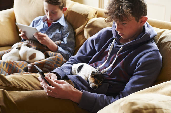 Boys using digital tablet and cell phone with puppies sleeping in laps — Stock Photo