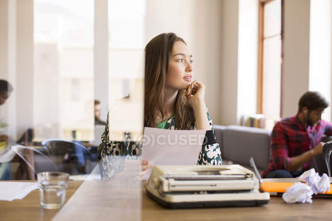 Pensive креативна бізнес-леді з паперовою роботою в друкарській машинці в офісі — стокове фото