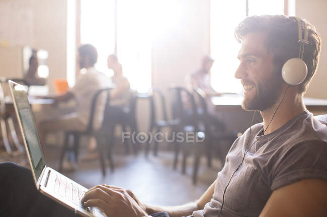Случайный бизнесмен в наушниках и работает за ноутбуком в офисе — стоковое фото