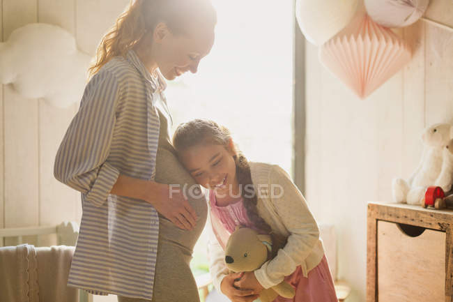 Hija escuchando el estómago de la madre embarazada en la guardería - foto de stock