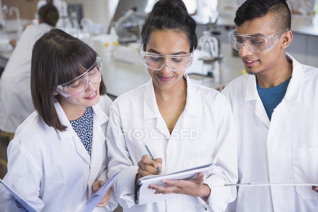 Studenten in Laborkitteln diskutieren im Klassenzimmer des Wissenschaftslabors über Notizen — Stockfoto